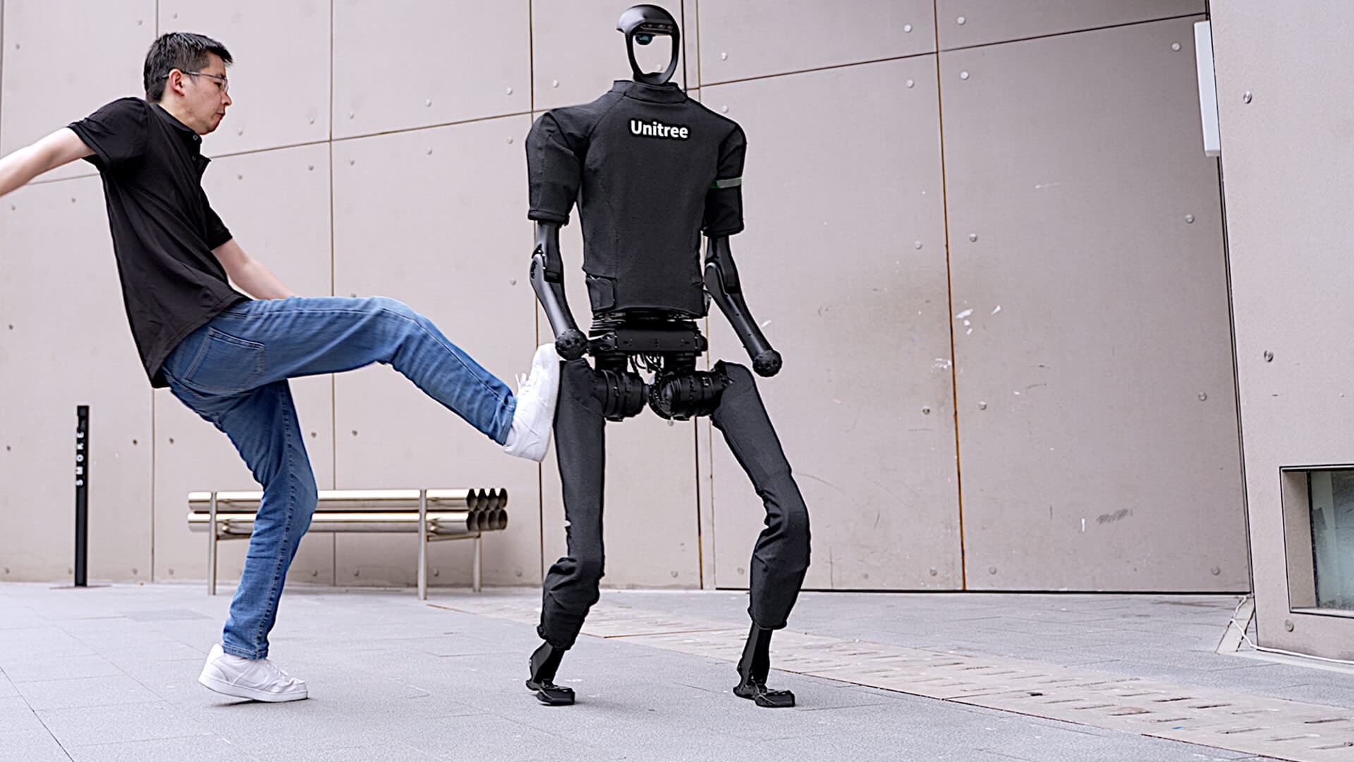 A man kicking a Unitree H1 humanoid robot, which stays upright