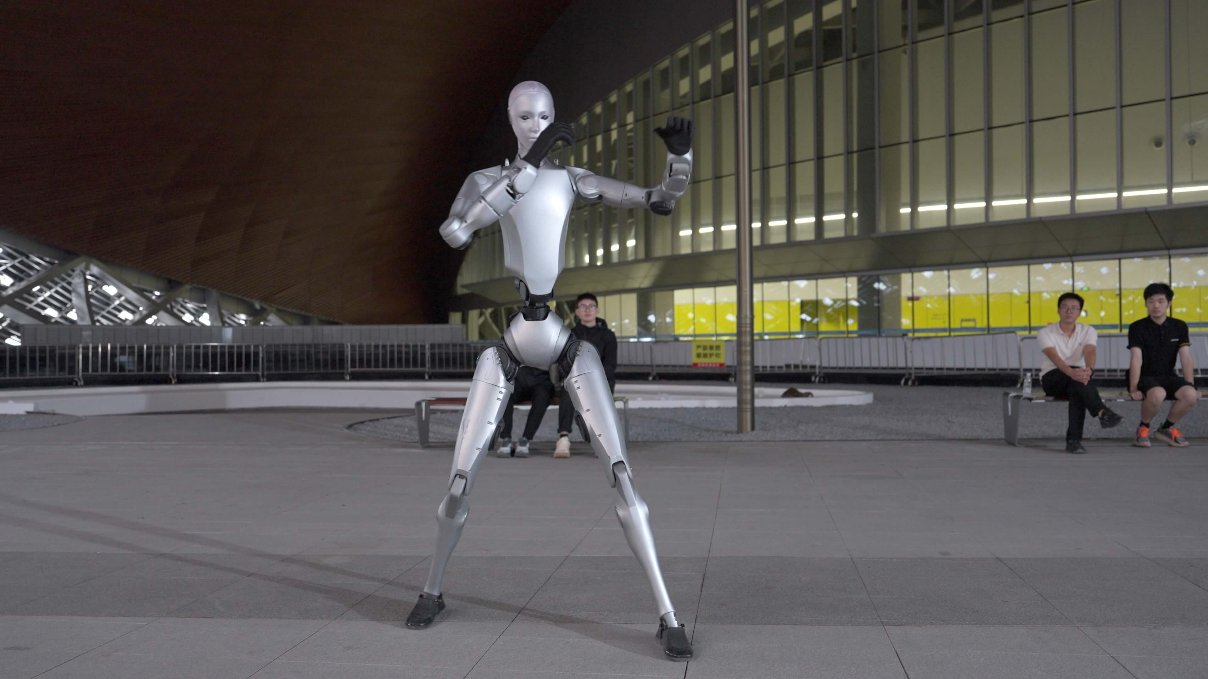 Unitree H2 humanoid robot standing in a boxing guard outside a stadium at night